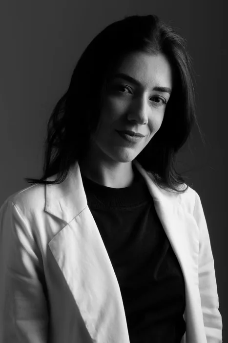 Portrait of a confident young woman with a stylish look and curly hair against a white backdrop.