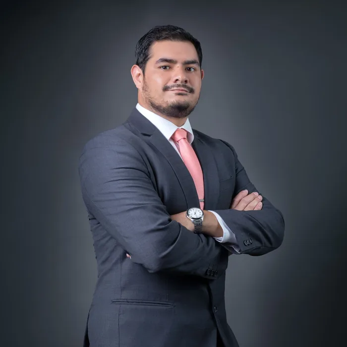 Professional portrait of a confident businessman in a gray suit with a pink tie, posing with arms crossed.