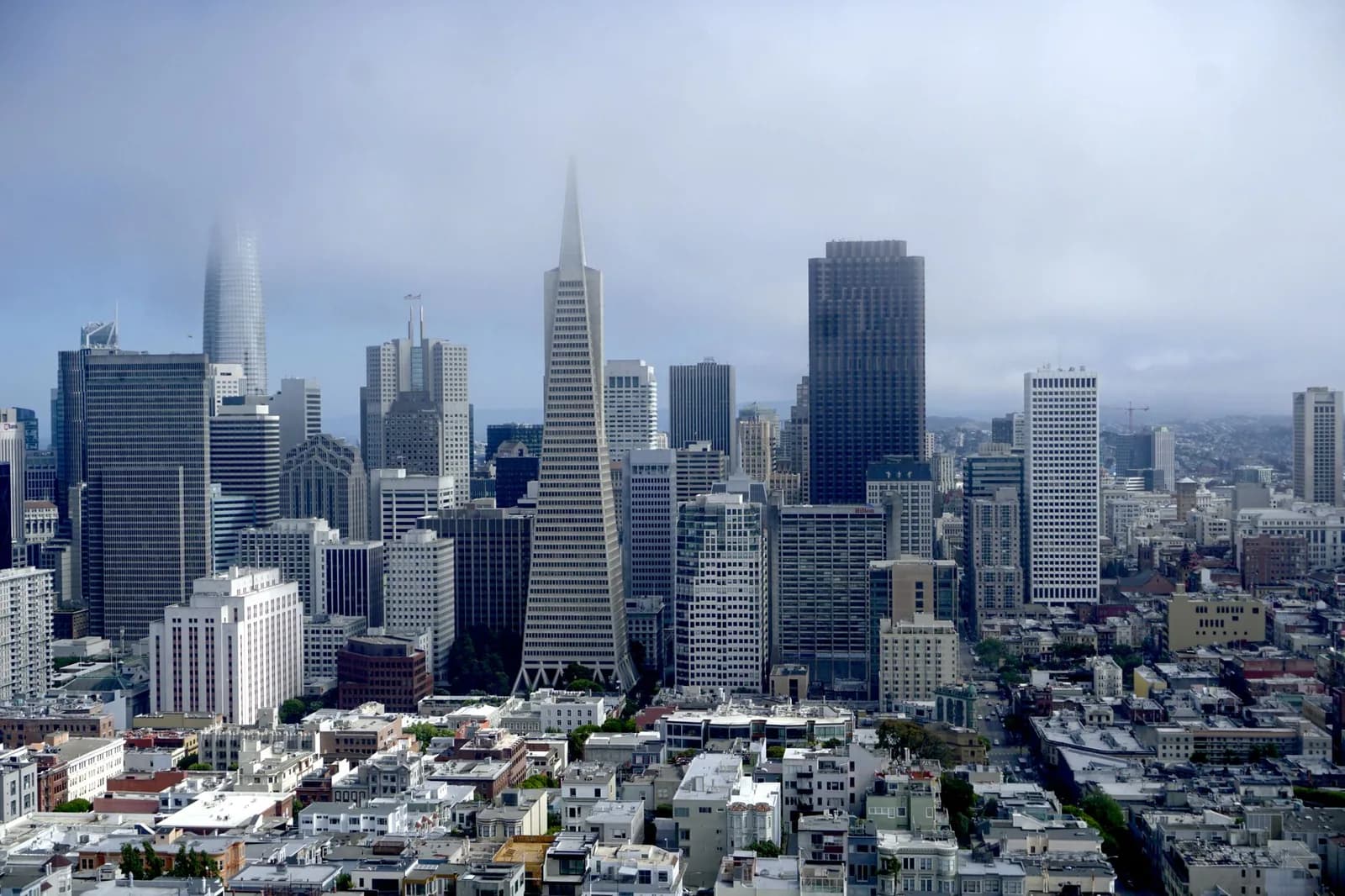 Panoramic aerial view of San Francisco's iconic skyline with fog and clouds.
