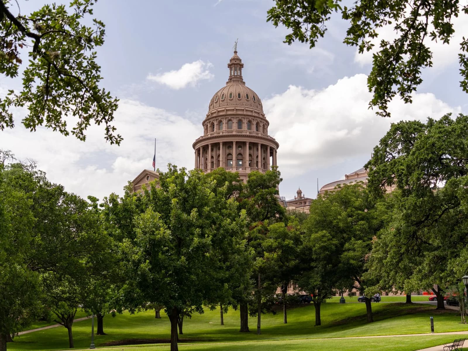 View of the Texas State Capitol dome amidst lush greenery on a sunny day in Austin.