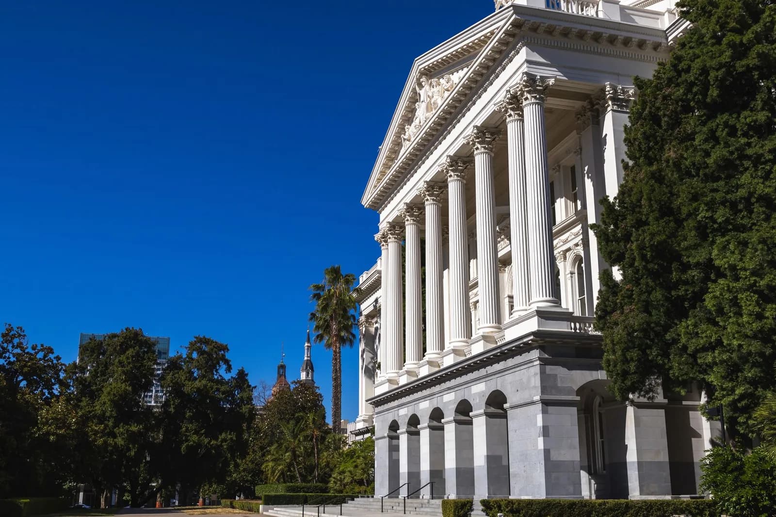 Beautiful sunlit view of the California State Capitol building with classic columns and vibrant blue sky.