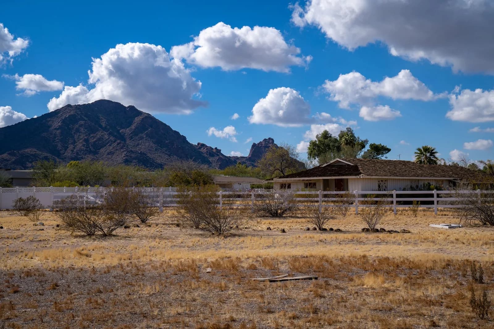 Charming rural farmhouse set against Arizona's stunning mountain scenery, under a bright blue sky.